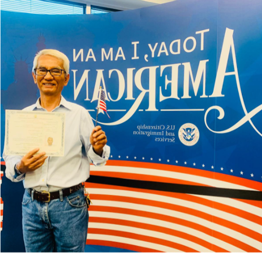 a man holding a tiny American flag and a certificate in front of a backdrop saying 